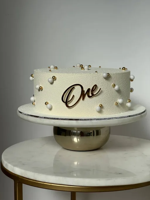 Gâteau blanc de premier anniversaire avec topper « One » et perles dorées